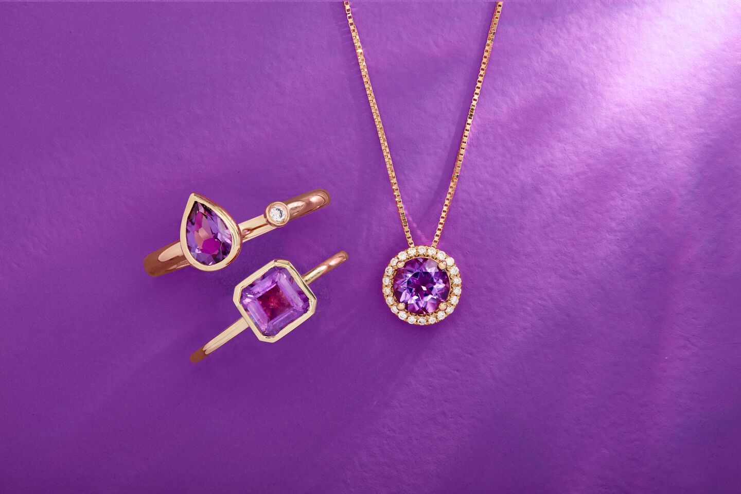 Purple gemstone jewelry rings and necklace are shown in 14K yellow gold with a purple background. 